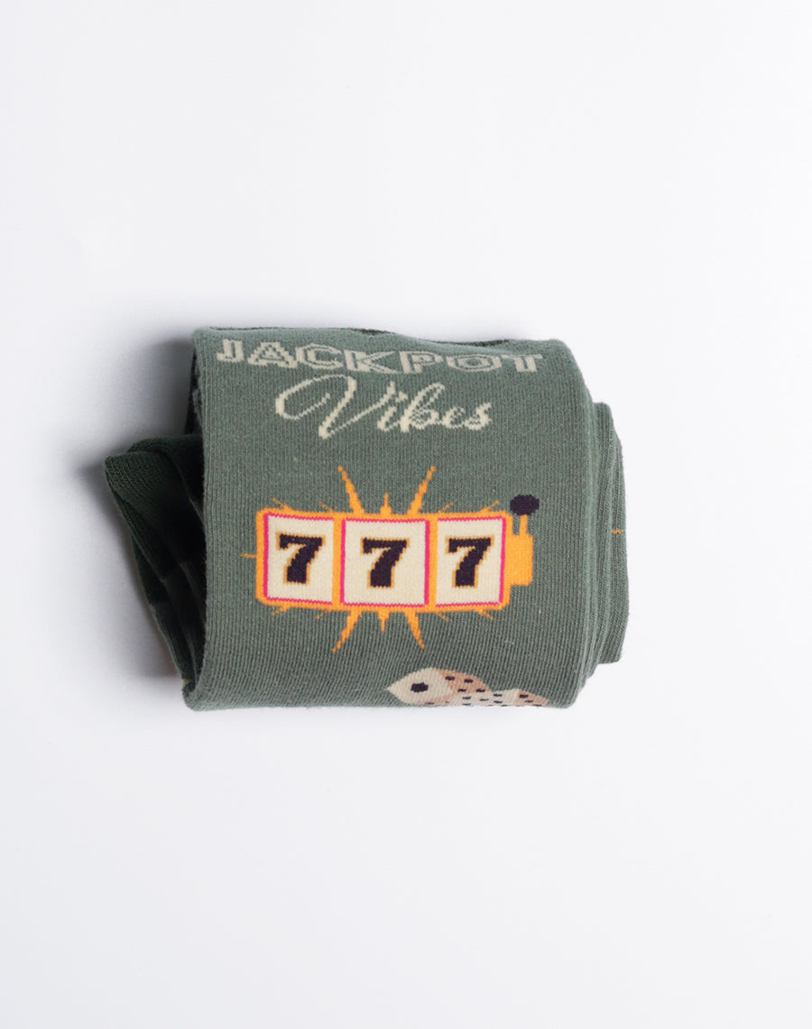 Fun men's socks with a dark green base, highlighting Las Vegas-themed designs such as '777', cards, and dice.