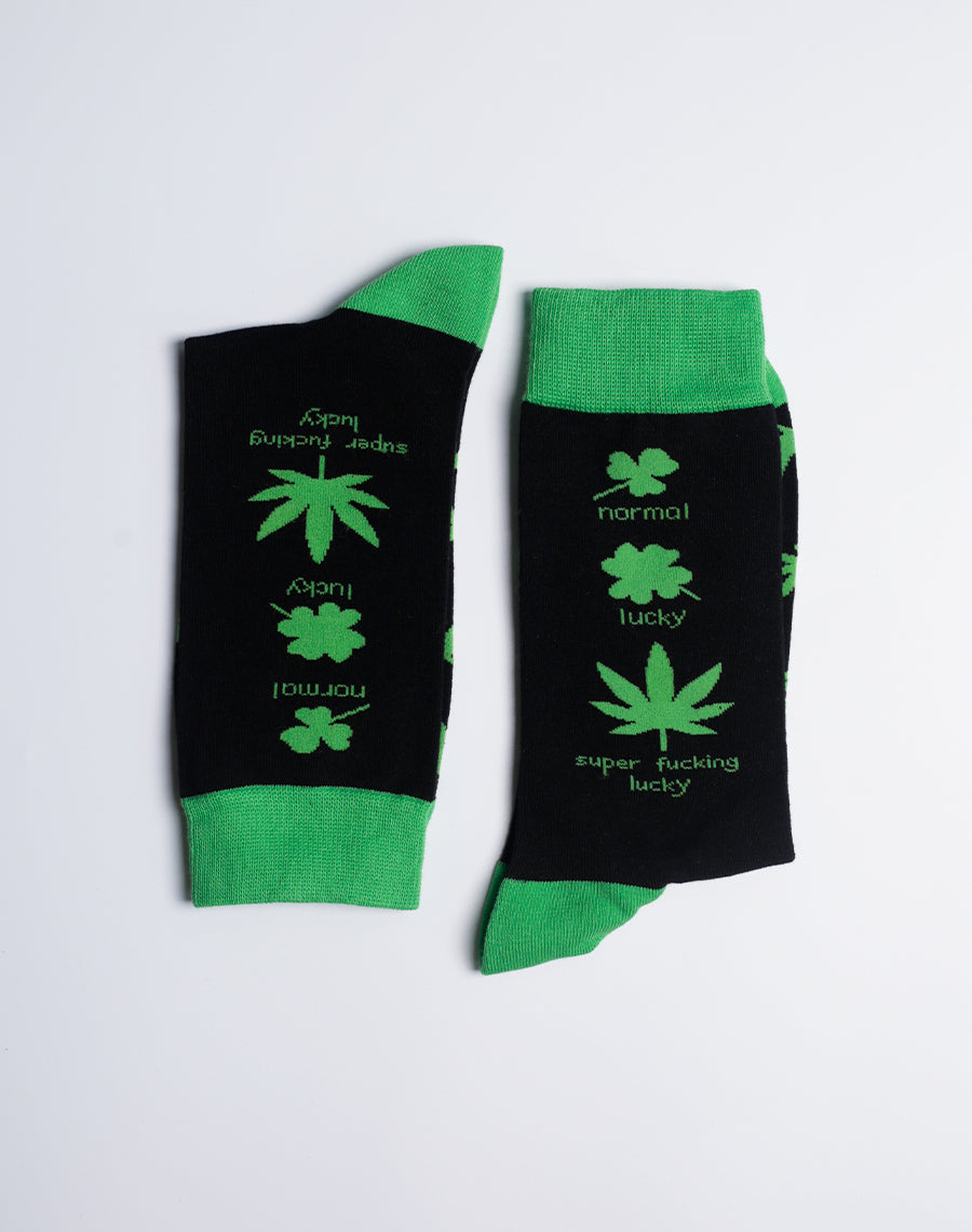 Men’s novelty crew socks featuring a repeating lucky weed leaf pattern in bright green against a sleek black fabric.
